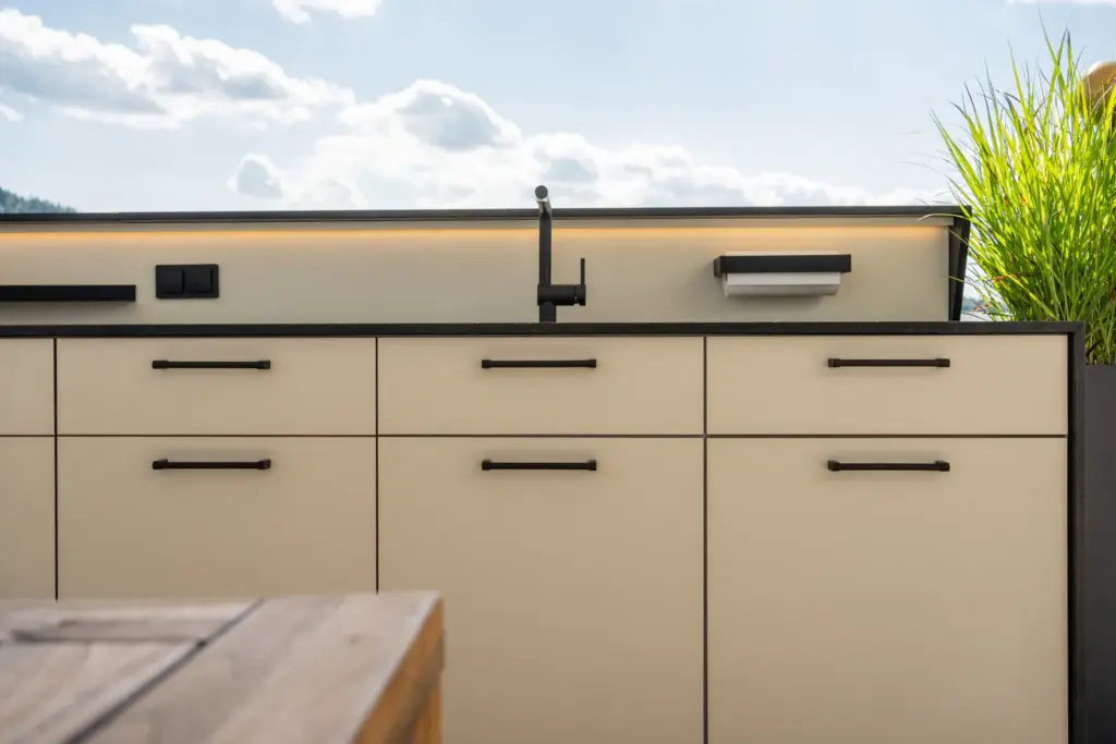 Detail der hellen Outdoorküche mit schwarzem Wasserhahn und Beleuchtung von Deutschmann