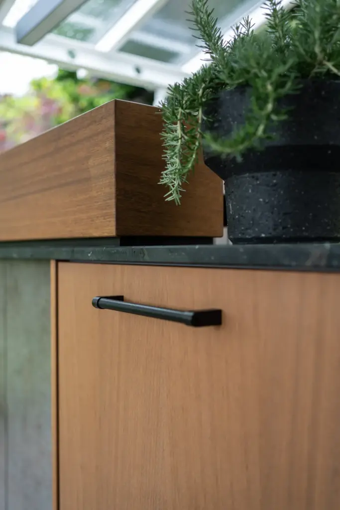 Detailaufnahme der Holzfront mit dunklem Griff und Kräutertopf auf der Arbeitsplatte