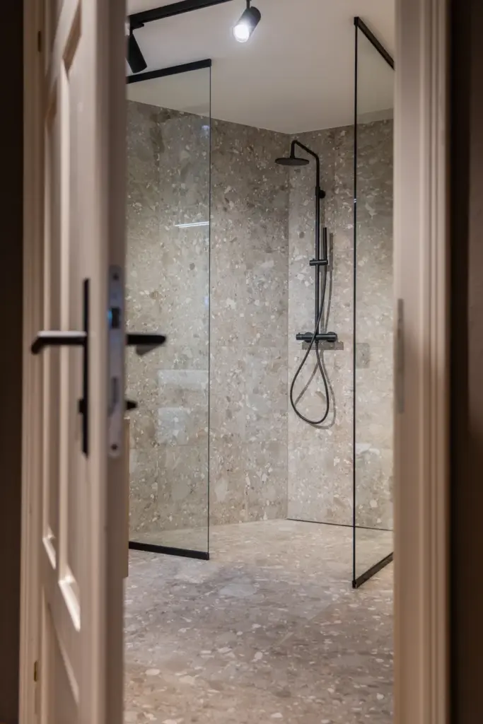 Großzügige Walk-in-Dusche mit Glaswänden und dunkler Armatur in Natursteinoptik umgesetzt von Deutschmann