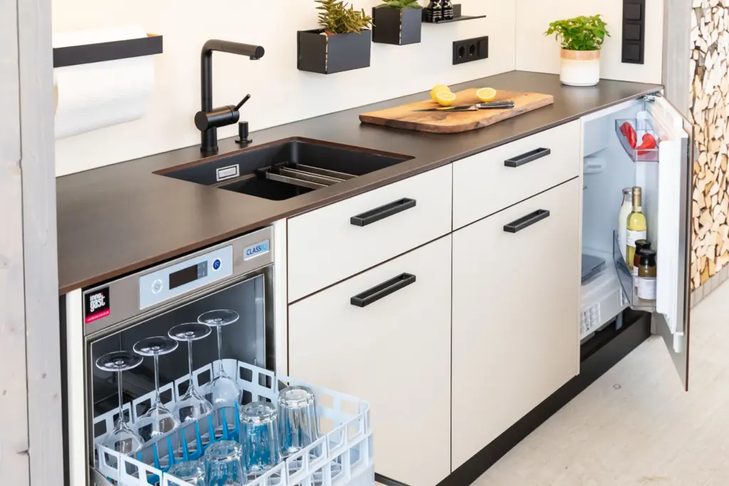 Maßgefertigte Outdoorküche von Deutschmann mit Geschirrspüler und integriertem Kühlschrank, sowie Spüle mit schwarzer Armatur