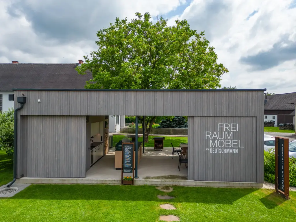 Moderne Ausstellung der Outdoormöbel von Deutschmann mit überdachter Outdoor Küche und Sitzbereich im Garten