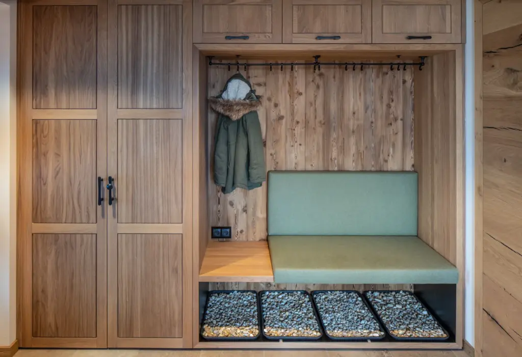 Maßgefertigte Garderobe aus Holz mit Sitzbank in grünem Stoff und Steinablagen im Eingangsbereich von Deutschmann