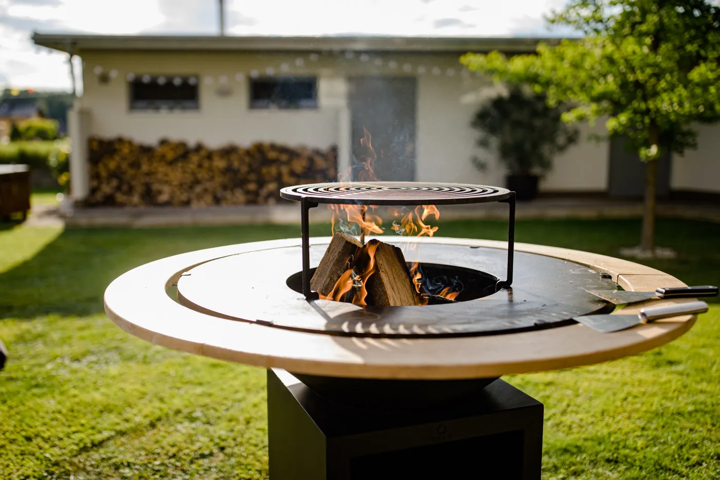 Moderner OFYR mit Flammen und Holzscheiten im Garten