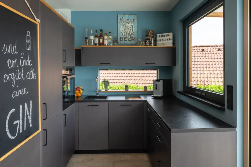 Moderne Küche in dunklen Farben mit hellblauer Wand und großem Fenster von Deutschmann