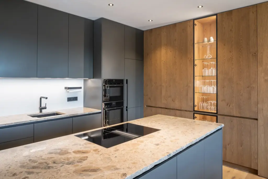 Moderne Küche mit Steinplatte Holzfronten und beleuchtetem Vitrinenschrank von Deutschmann