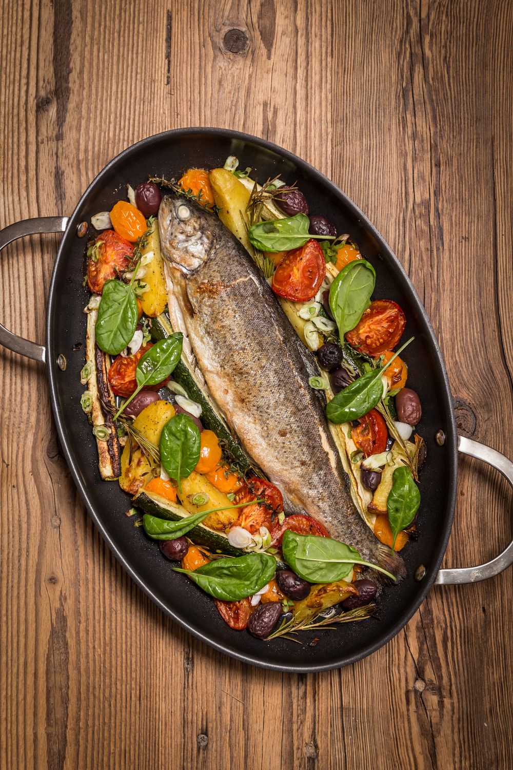 Draufansicht von einem Pfandl mit gerilltem Gemüse und einem fertigen Fisch drauf