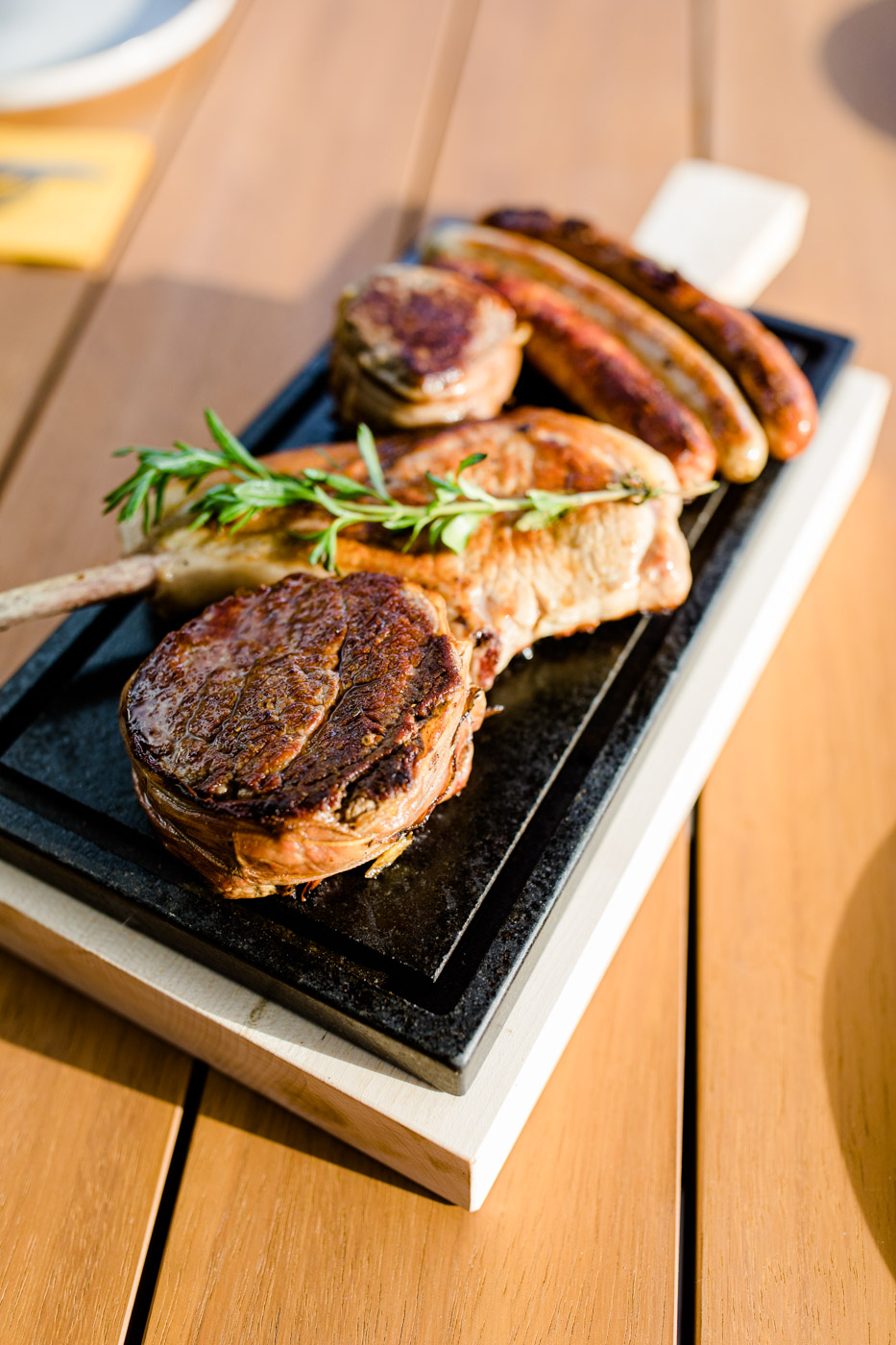 Draufansicht von einem Brett auf einem Tisch, wo diverses gegrilltes Fleisch und Würstl zu sehen sind