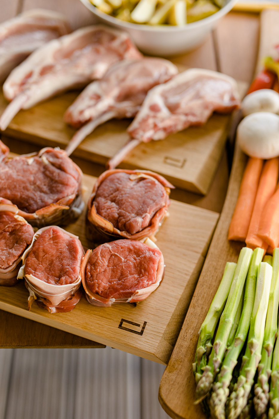 Draufansicht von untereschiedlich, befüllten Brettln. Rohes unterschiedliches Fleisch und Gemüse wie Karotten, Spargel und Pilze drauf