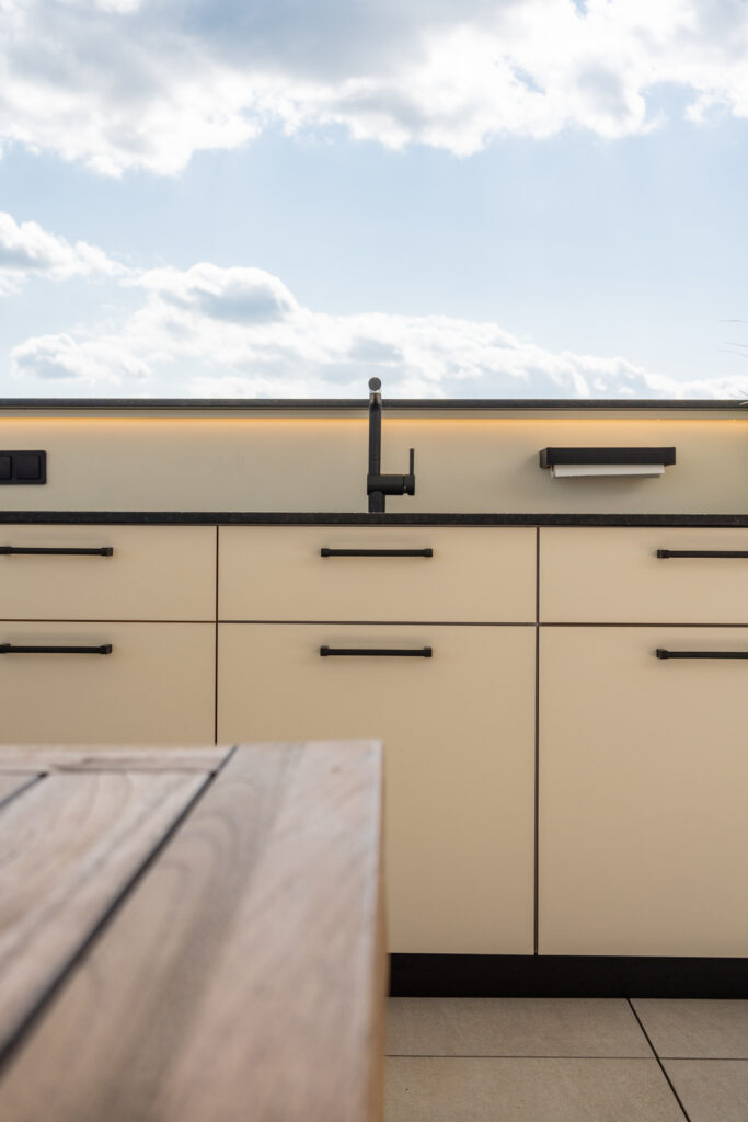 Detailansicht einer Outdoorküche mit schwarzen Griffen und weißer Front, Detailfoto auf schwarzem Wasserhahn