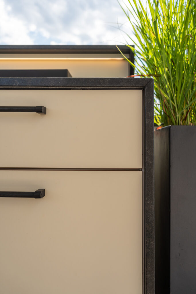 Detailansicht einer weißen Outdoorküche mit schwarzen Griffen und LED-Leiste