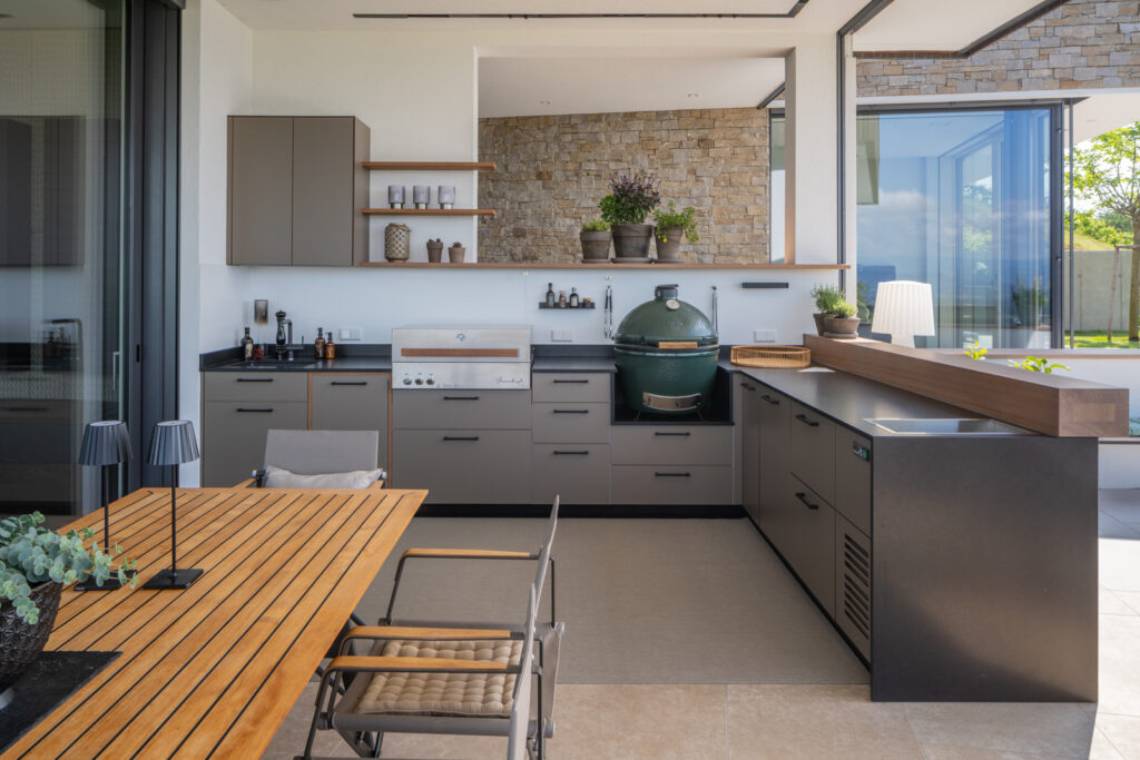 Graue Eck-Outdoorküche mit schwarzer Arbeitsfläche und integriertem Flammkraft Gasgrill sowie Big Green Egg Grill