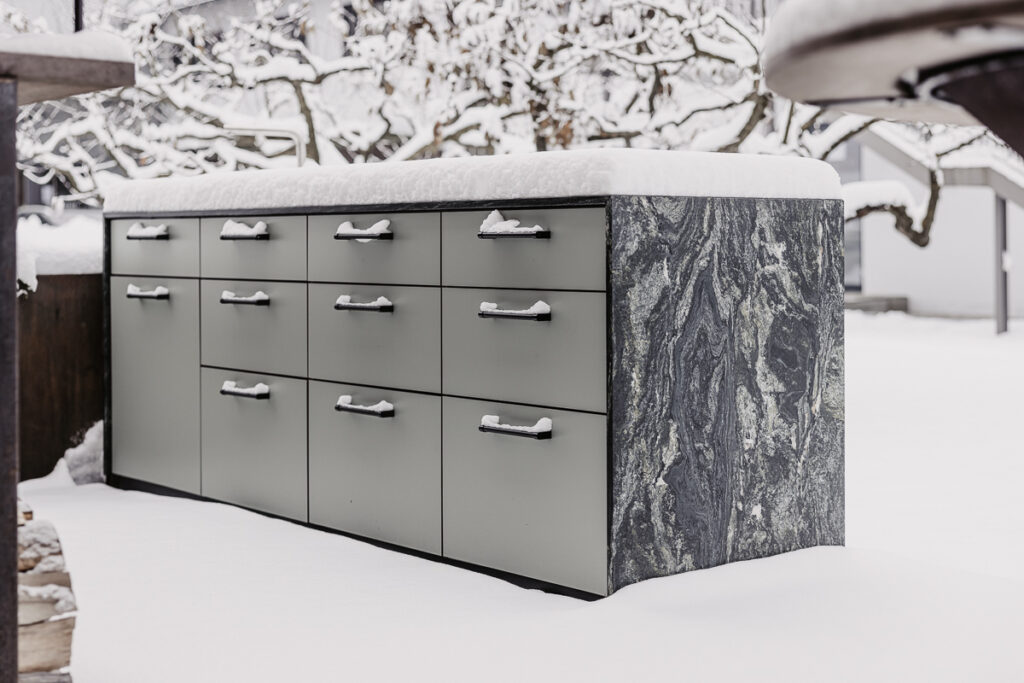 Grüne Outdoorküche mit Marmor-Arbeitsfläche welche aber mit dichtem Schnee bedeckt ist, schwarze Griffe, welche ebenso voll Schnee sind