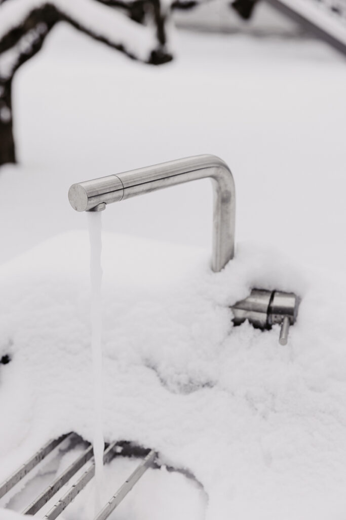Detailansicht eines Wasserhahns welcher voll umgeben von Schnee ist und in einer Schnee bedeckten Outdoorküche integriert ist