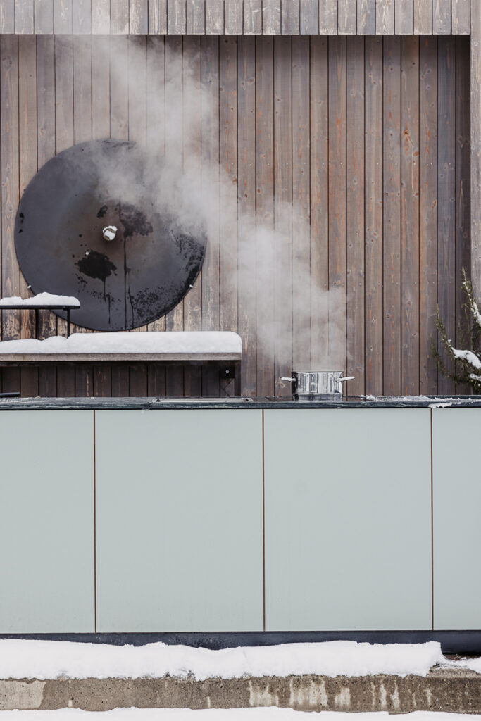 Outdoorküche mit grüner Front und Marmorarbeitsfläche, darauf steht ein dampfender Topf mit Wasser
