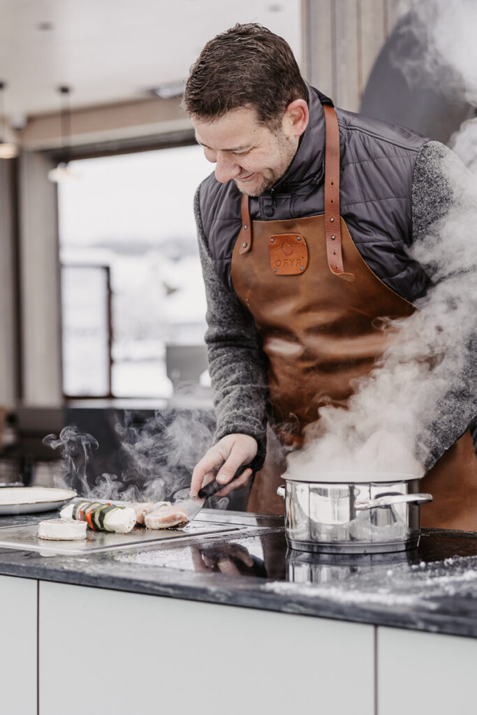 Sepp Deutschmann grillt und kocht auf der Plug & Play Outdoorküche, Gemüsespieße und Fleisch auf dem Teppanyakigrill und ein dampfender Kochtopf auf dem Indu+ Kochfeld daneben
