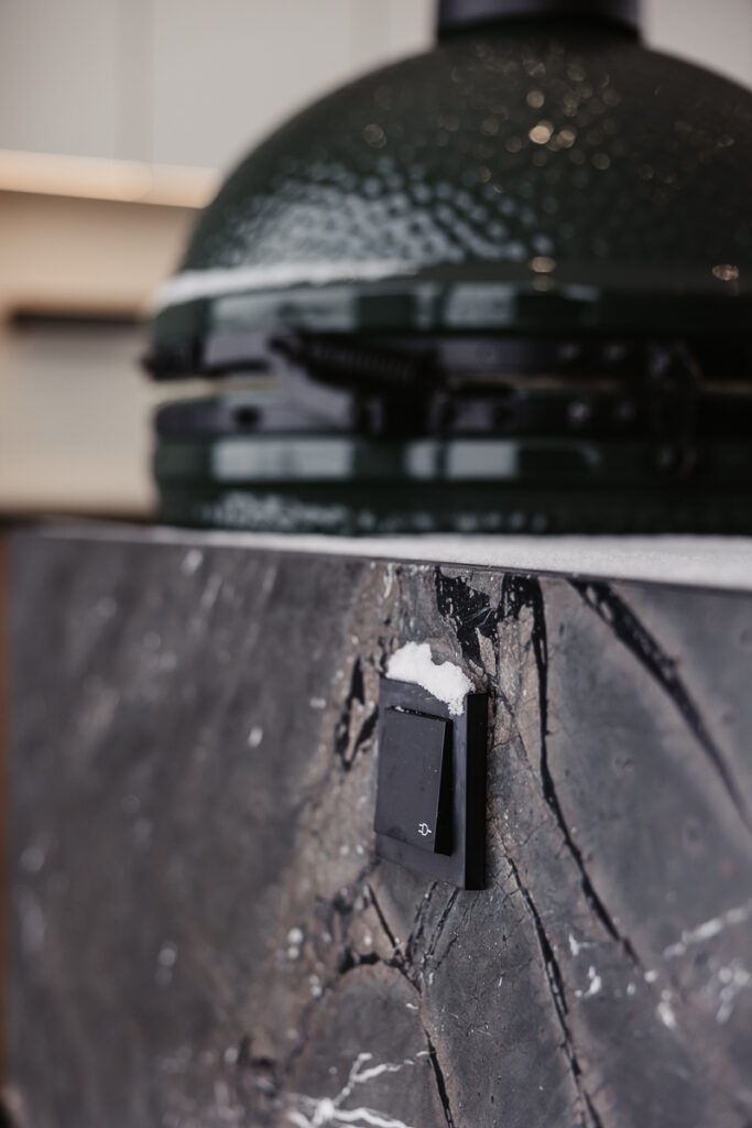 Detailansicht des Big Green Egg Grills welcher in einer Outdoorküche von Deutschmann integriert ist, mit Fokus auf eine daneben platzierte Steckdose