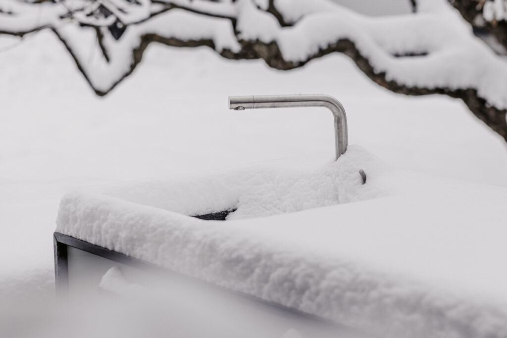 Detailansicht eines Wasserhahns welcher voll umgeben von Schnee ist und in einer Schnee bedeckten Outdoorküche integriert ist