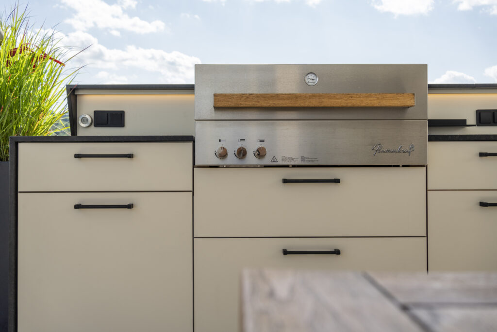 Detailansicht einer weißen Outdoorküche mit schwarzen Griffen und einem integrierten Flammkraft Gasgrill