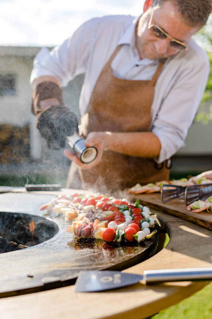 Grillbuddy, Holzring von Deutschmann rund um den OFYR Grill, dient als Ablagefläche für Grillutensilien, am Grill befinden sich Tomaten Mozarella Sticks